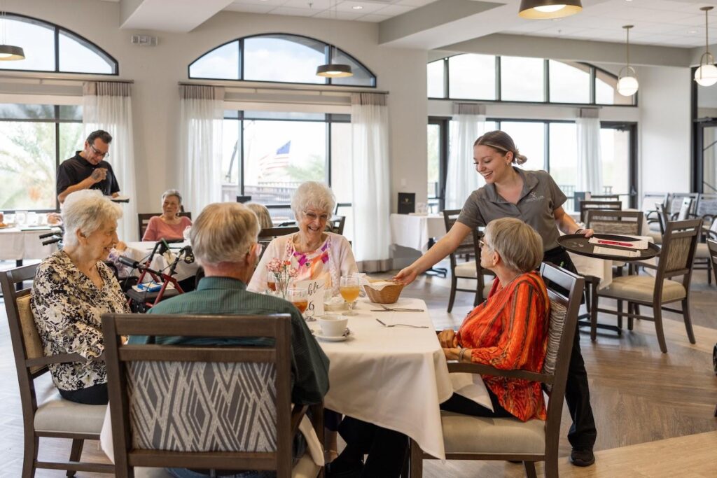 Four senior residents sitting down for lunch at Fountain View Village while being served by a smiling server.